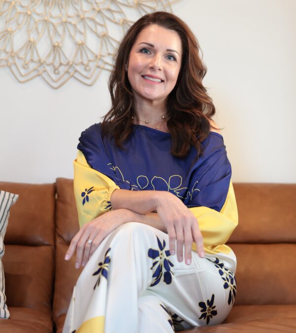 Layla, the practitioner at Park Circle Head Spa, sitting on a brown sofa in a blue and yellow outfit