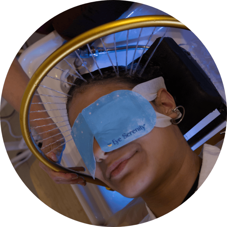 Client lying back at the basin with an eye mask on while a gold ring sprays fine streams of water over her scalp