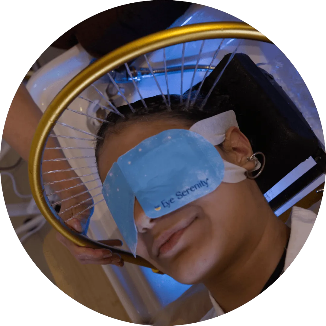 Client lying back at the basin with an eye mask on while a ring of fine water streams rinses her scalp